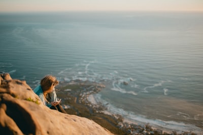 女人穿着灰色衬衫坐在悬崖附近的海洋
